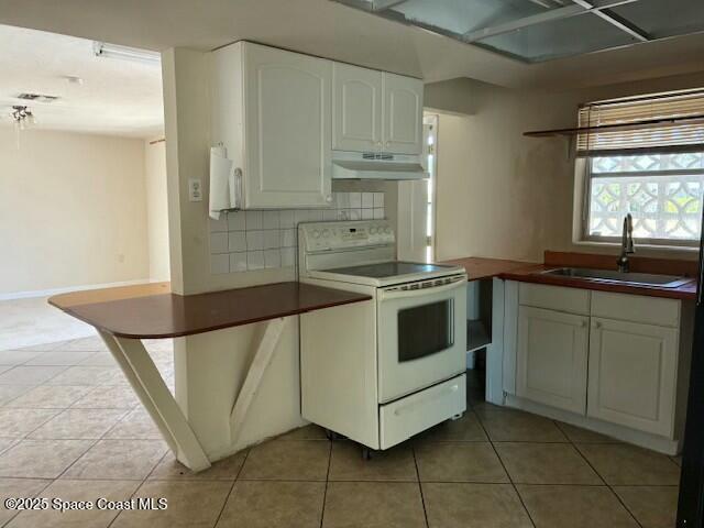 kitchen featuring light tile patterned floors, under cabinet range hood, a sink, white cabinetry, and white electric range