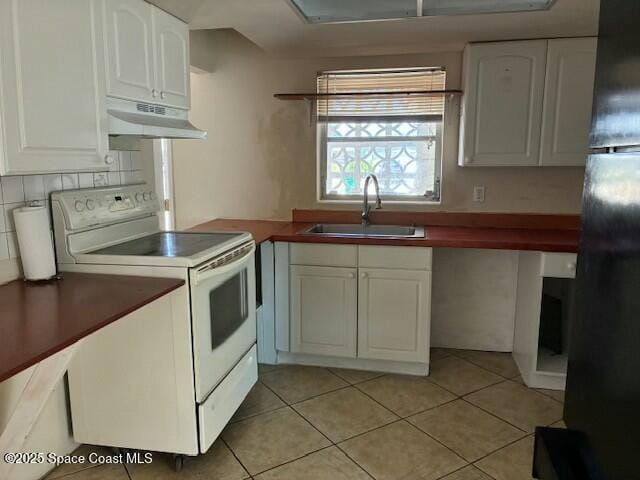 kitchen featuring a sink, under cabinet range hood, white cabinets, freestanding refrigerator, and electric range