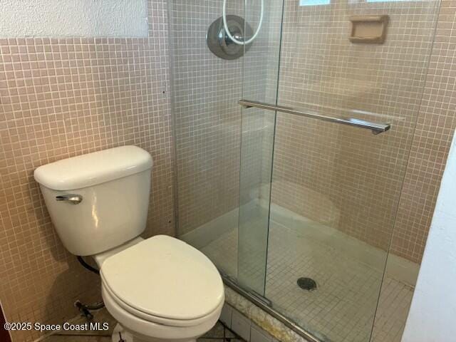 bathroom with toilet, a stall shower, and tile walls