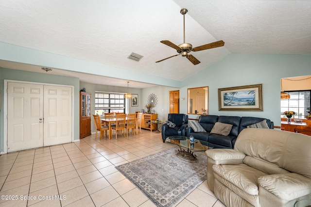 living room with ceiling fan, lofted ceiling, light tile patterned floors, and a textured ceiling