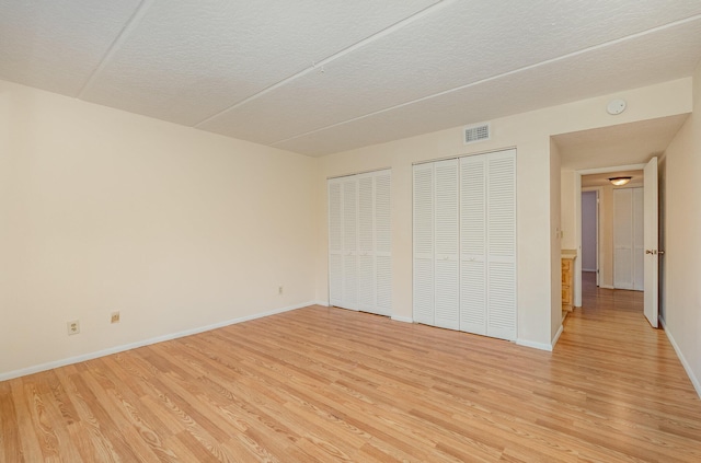 unfurnished bedroom featuring multiple closets and light wood-type flooring