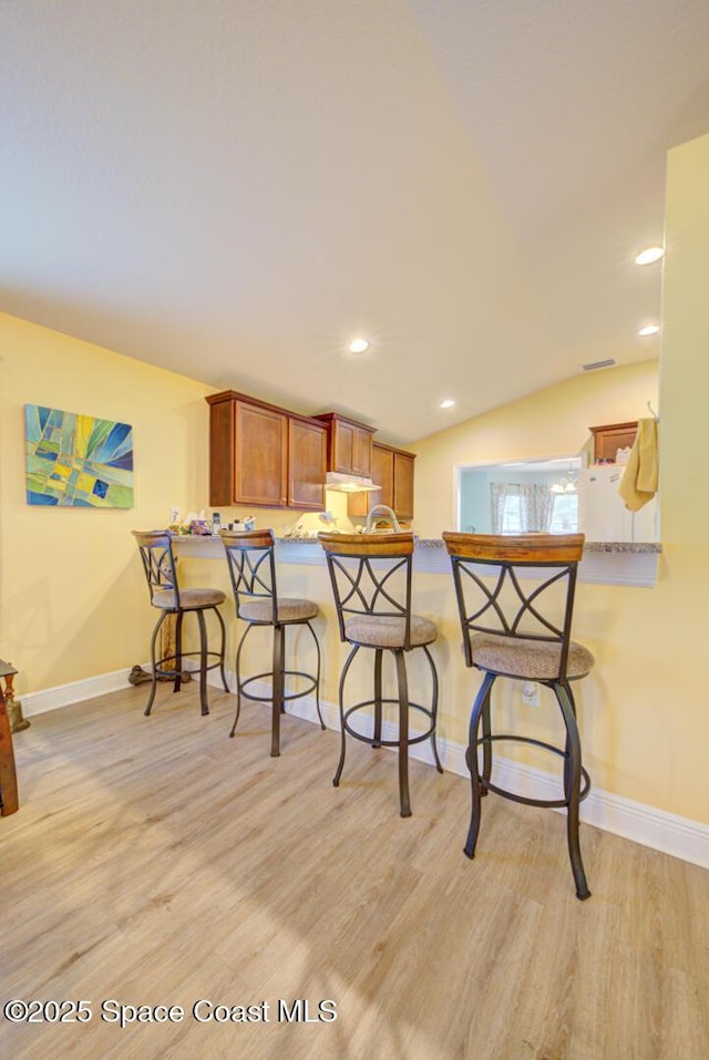 kitchen with light wood-type flooring, vaulted ceiling, and kitchen peninsula