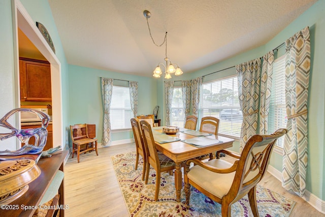 dining space featuring a textured ceiling, light hardwood / wood-style flooring, a notable chandelier, and vaulted ceiling