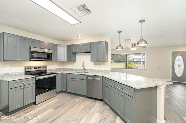 kitchen with pendant lighting, appliances with stainless steel finishes, sink, gray cabinetry, and light hardwood / wood-style floors