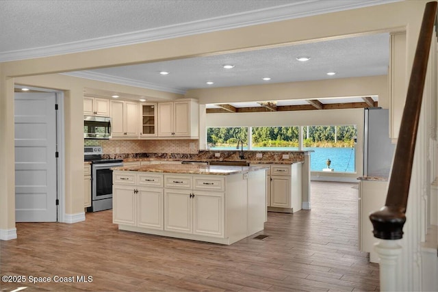 kitchen featuring stainless steel appliances, light stone countertops, cream cabinets, and a center island