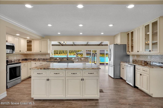 kitchen featuring a kitchen island, appliances with stainless steel finishes, hardwood / wood-style floors, tasteful backsplash, and light stone counters