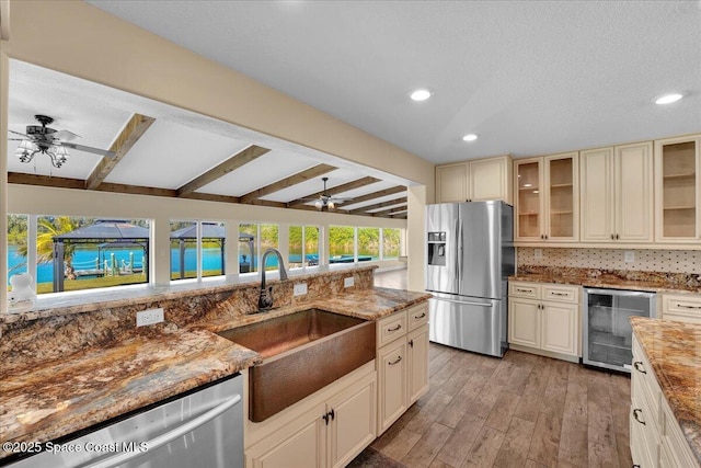 kitchen featuring cream cabinetry, beam ceiling, beverage cooler, and appliances with stainless steel finishes