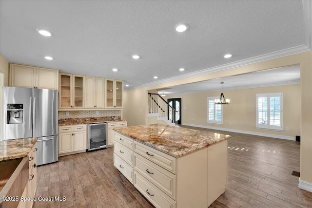 kitchen featuring hanging light fixtures, stainless steel refrigerator with ice dispenser, beverage cooler, a kitchen island, and cream cabinetry