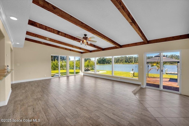 unfurnished living room with a textured ceiling, lofted ceiling with beams, ceiling fan, and a water view