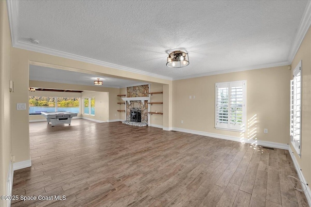 unfurnished living room featuring hardwood / wood-style flooring, a stone fireplace, a textured ceiling, and crown molding