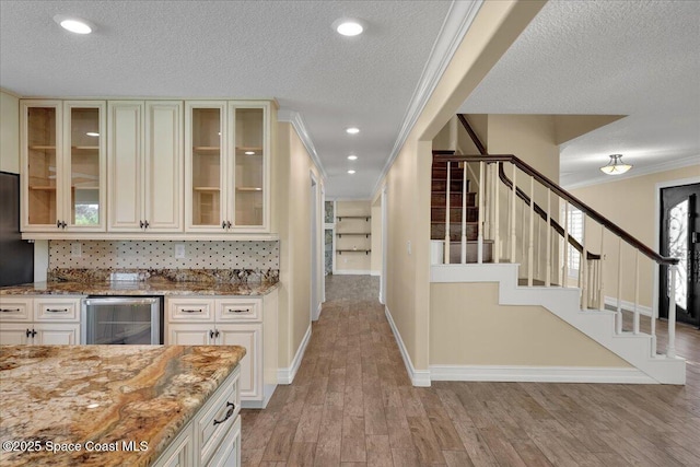 kitchen featuring light wood-type flooring, wine cooler, ornamental molding, light stone countertops, and a textured ceiling