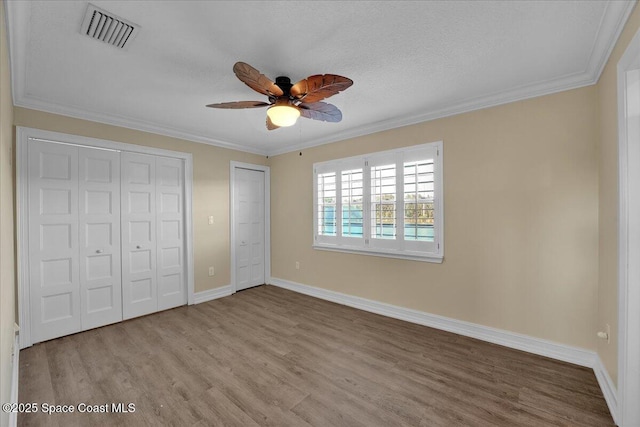 unfurnished bedroom featuring multiple closets, crown molding, light hardwood / wood-style floors, and ceiling fan