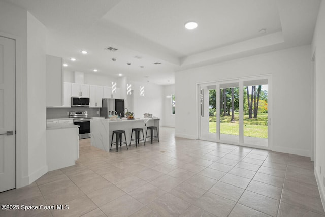 kitchen featuring white cabinets, a kitchen island, a raised ceiling, a breakfast bar, and stainless steel appliances