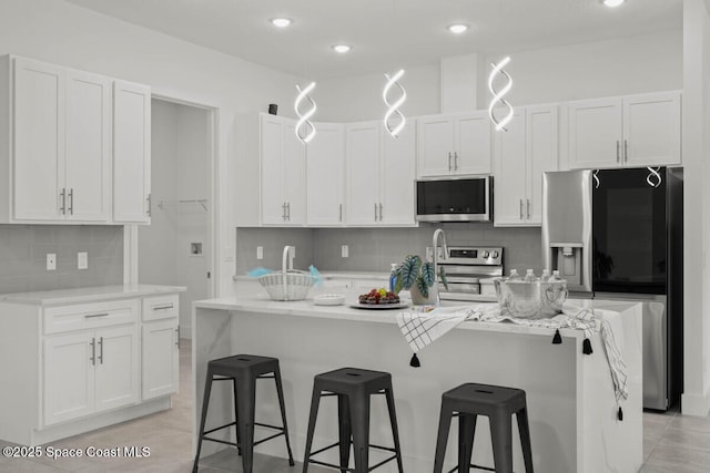 kitchen with a breakfast bar, white cabinetry, appliances with stainless steel finishes, and an island with sink