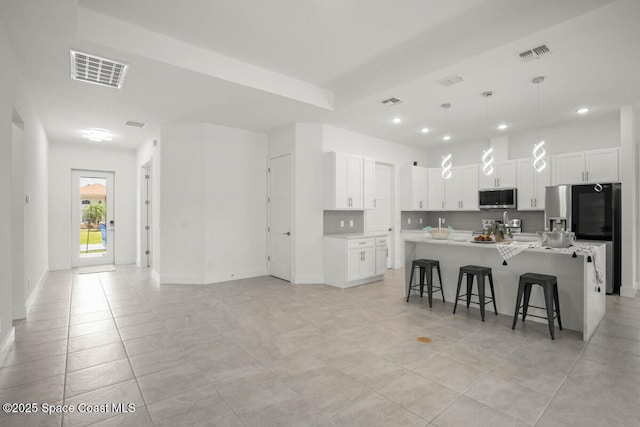 kitchen featuring appliances with stainless steel finishes, white cabinetry, a kitchen breakfast bar, decorative light fixtures, and a center island with sink