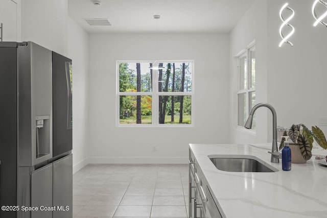 kitchen featuring light stone countertops, decorative light fixtures, a healthy amount of sunlight, sink, and stainless steel fridge with ice dispenser