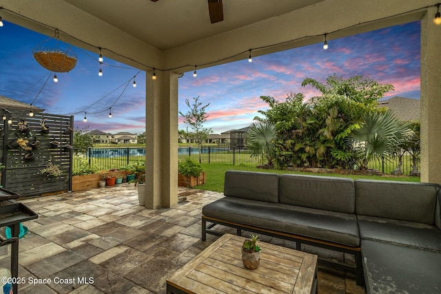 patio terrace at dusk featuring ceiling fan, outdoor lounge area, and a water view