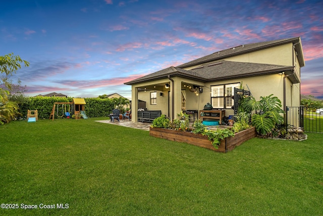 back house at dusk with a patio area, a yard, and a playground