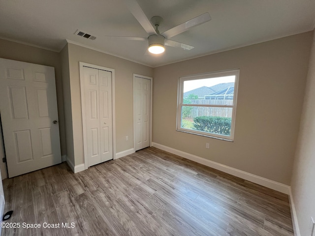 unfurnished bedroom with crown molding, ceiling fan, light wood-type flooring, and two closets