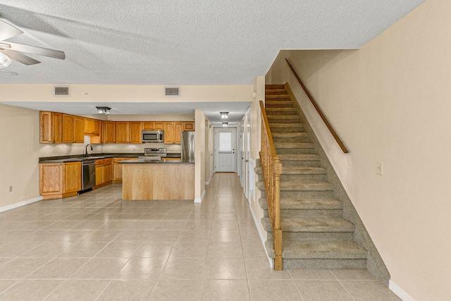 kitchen with appliances with stainless steel finishes, a kitchen island, sink, light tile patterned flooring, and ceiling fan