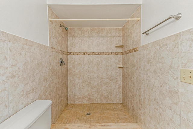 bathroom with a tile shower, toilet, and tile walls