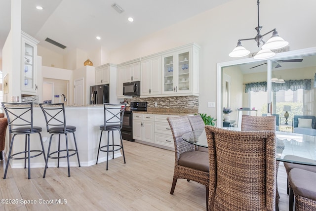 kitchen with light stone countertops, pendant lighting, black appliances, white cabinetry, and decorative backsplash