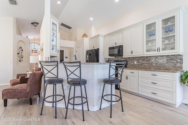 kitchen with black appliances, dark stone countertops, white cabinets, and backsplash