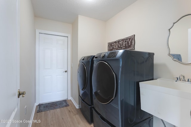 clothes washing area featuring sink, a textured ceiling, light hardwood / wood-style flooring, and washing machine and clothes dryer