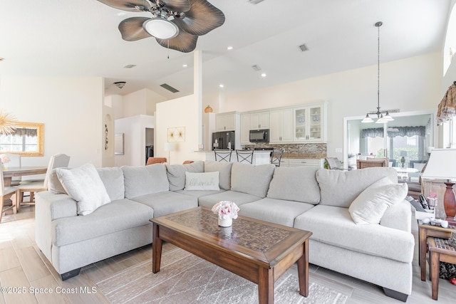 living room with high vaulted ceiling, ceiling fan, and light wood-type flooring