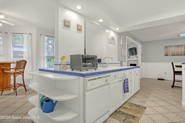 kitchen featuring white dishwasher, sink, white cabinets, light tile patterned flooring, and tile counters