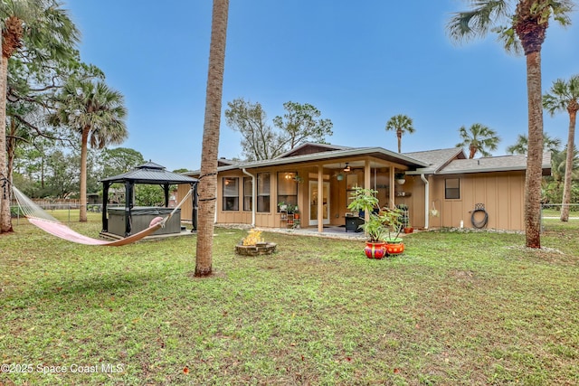 back of property with a lawn, an outdoor fire pit, a gazebo, and a hot tub