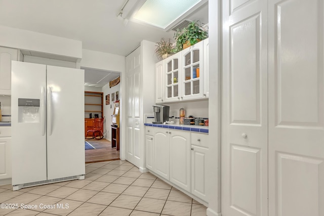 kitchen featuring white cabinetry, white fridge with ice dispenser, light tile patterned floors, and tile countertops