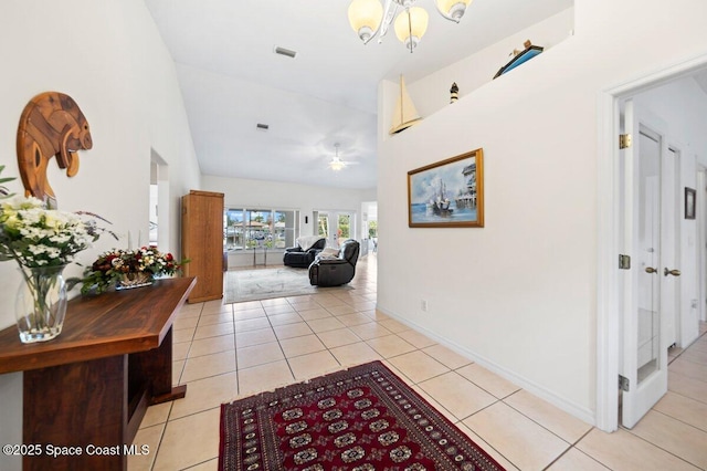 hallway with light tile patterned floors, baseboards, visible vents, an inviting chandelier, and lofted ceiling