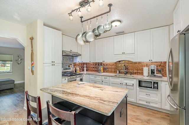 kitchen featuring sink, white cabinetry, light stone counters, stainless steel appliances, and backsplash