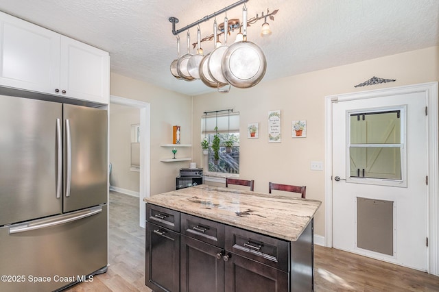 kitchen with white cabinetry, light wood-type flooring, stainless steel fridge, light stone counters, and a textured ceiling