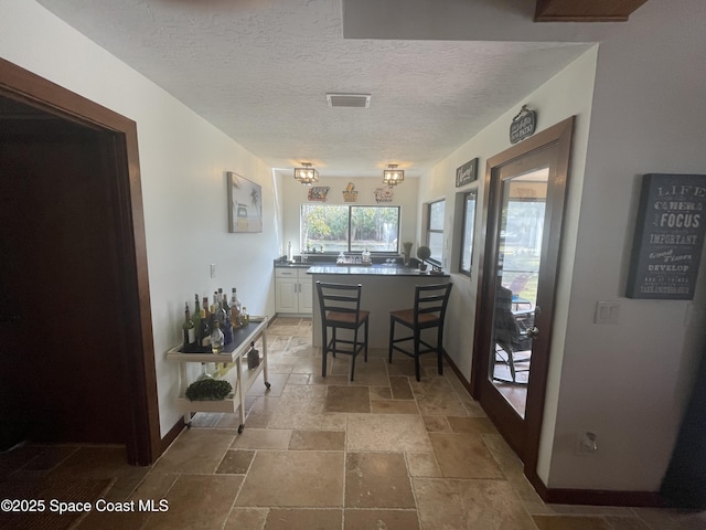 dining area with baseboards, visible vents, a textured ceiling, and stone tile floors