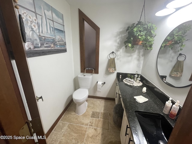 bathroom featuring double vanity, baseboards, toilet, stone finish floor, and a sink