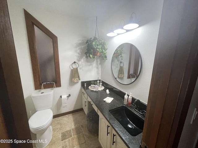 bathroom featuring double vanity, toilet, stone finish flooring, a sink, and baseboards