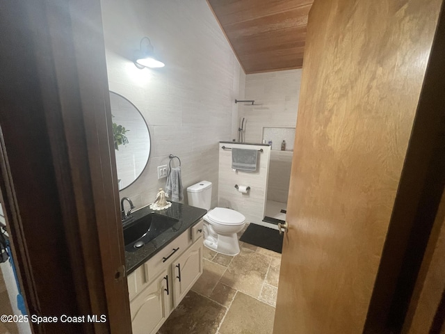 bathroom featuring stone tile floors, toilet, wood ceiling, vanity, and a walk in shower