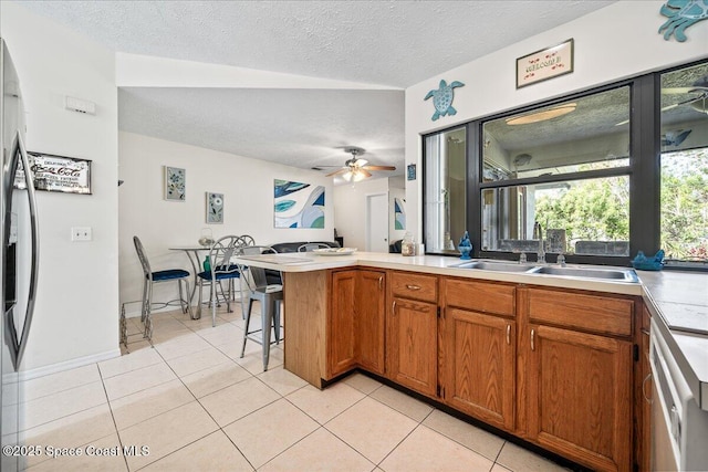 kitchen with sink, stainless steel refrigerator with ice dispenser, a textured ceiling, light tile patterned flooring, and kitchen peninsula