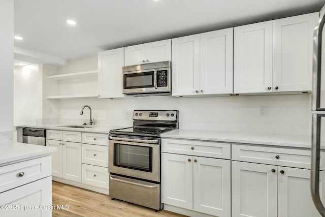 kitchen with sink, stainless steel appliances, white cabinetry, and light hardwood / wood-style floors