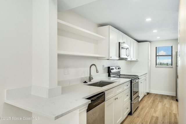 kitchen with appliances with stainless steel finishes, white cabinetry, sink, light wood-type flooring, and light stone counters