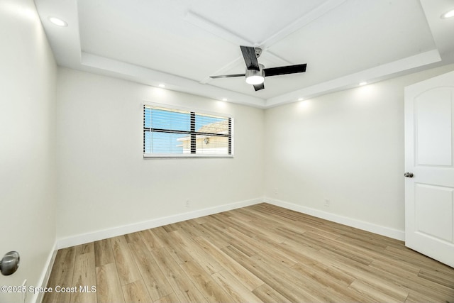 empty room featuring ceiling fan, a raised ceiling, and light wood-type flooring