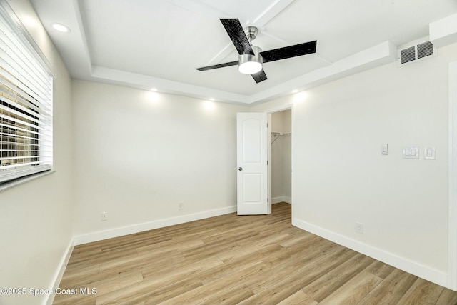 empty room with ceiling fan, light hardwood / wood-style flooring, and a tray ceiling