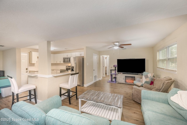 living room with a textured ceiling, ceiling fan, and light hardwood / wood-style flooring