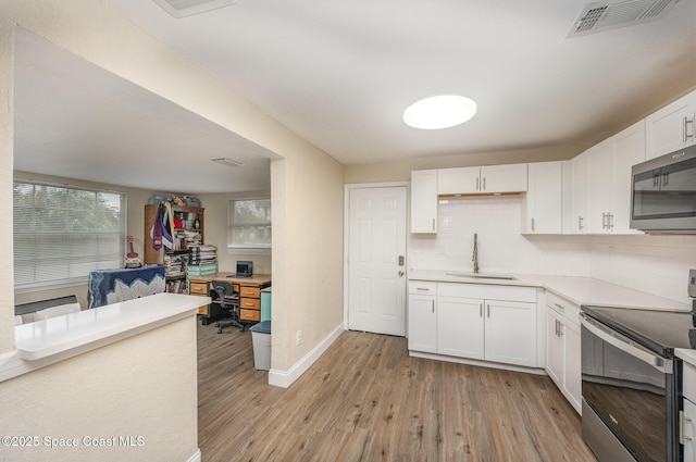 kitchen with appliances with stainless steel finishes, sink, white cabinets, decorative backsplash, and light hardwood / wood-style flooring