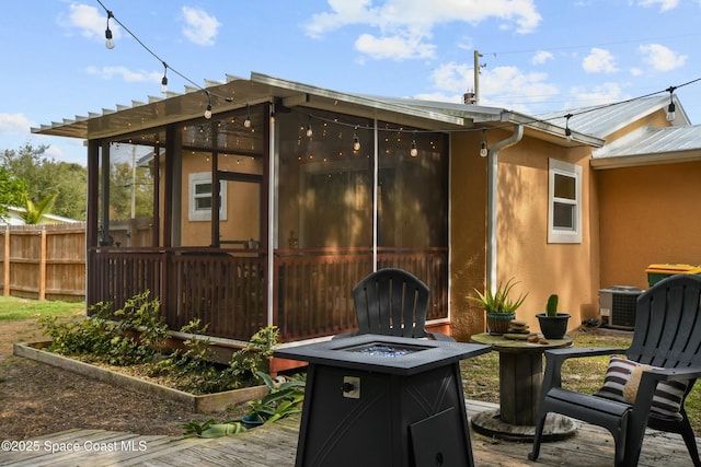 view of patio with a wooden deck, a sunroom, central air condition unit, and a fire pit