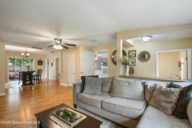 living room featuring ceiling fan with notable chandelier, light hardwood / wood-style flooring, and a textured ceiling