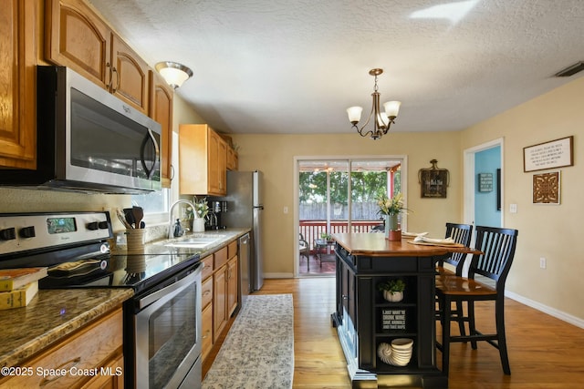 kitchen with pendant lighting, sink, dark stone counters, stainless steel appliances, and light hardwood / wood-style flooring