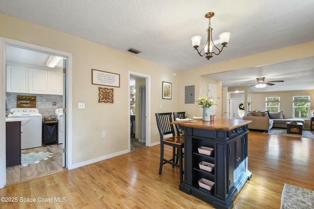 dining space featuring washing machine and dryer, electric panel, light hardwood / wood-style floors, a textured ceiling, and ceiling fan with notable chandelier